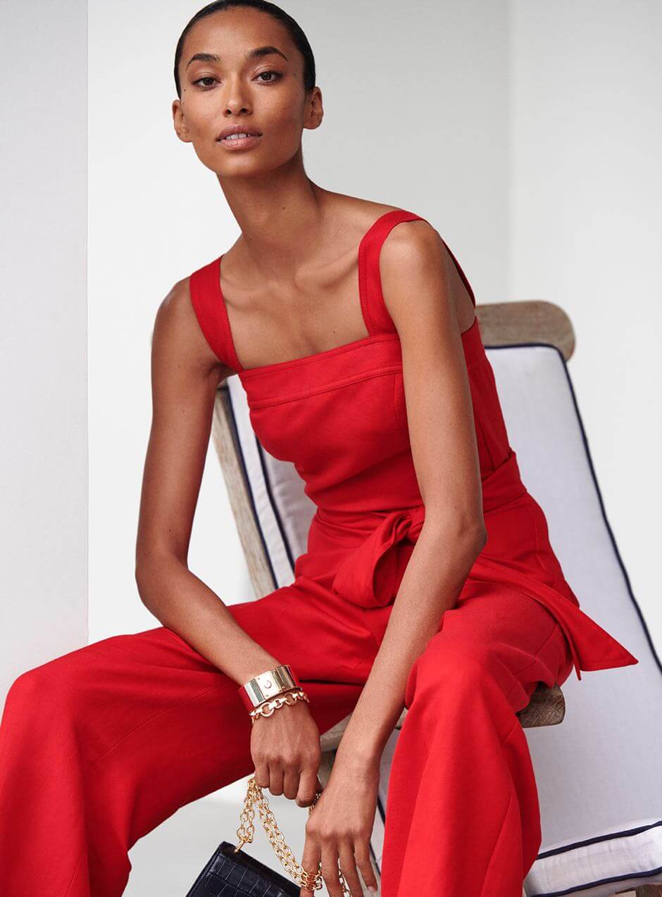 Woman wears red tie-waist jumpsuit.