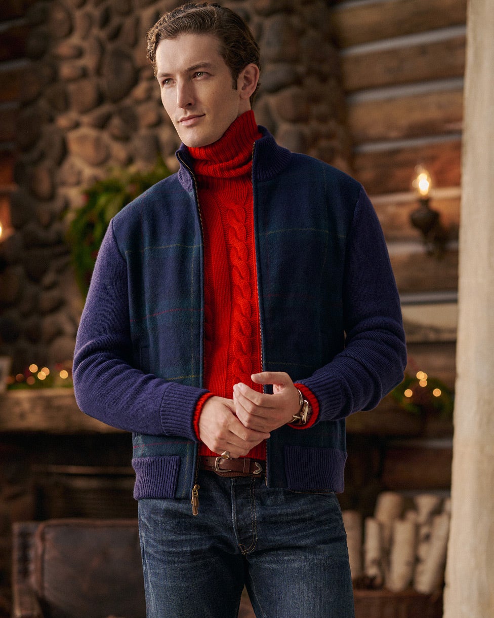Mann in rotem Rollkragenpullover mit Zopfmuster, marineblauer Jacke und Jeans.