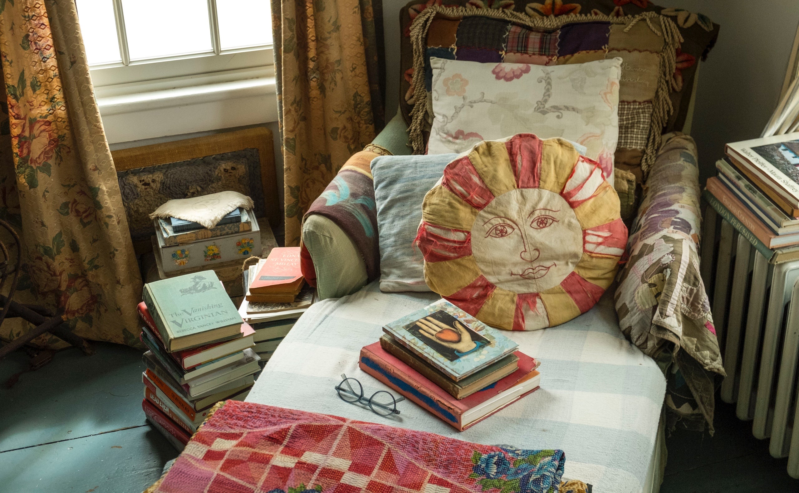 Ein gem&uuml;tliches Sofa im Schlafzimmer, umgeben von B&uuml;chern und mit einer sonnengeblichenen Decke, Steppdecken und anderen weichen Textilien sowie einem bunten Mix an Vintage-Kissen