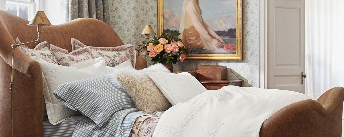 Photograph of bed made with linens in white, stripes, and floral patterns.