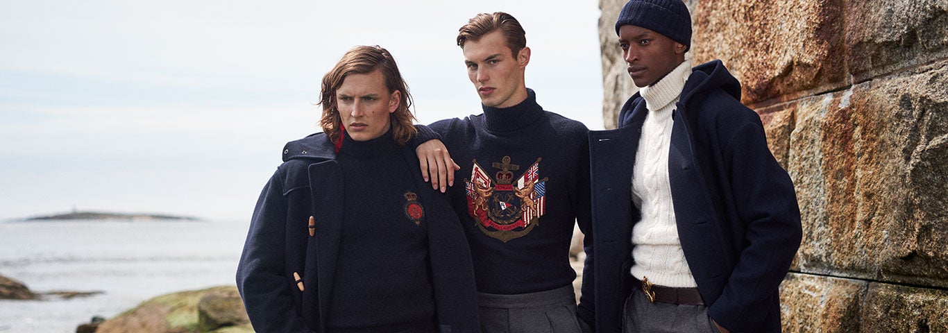 Three men in naval-inspired styles stand by rock wall